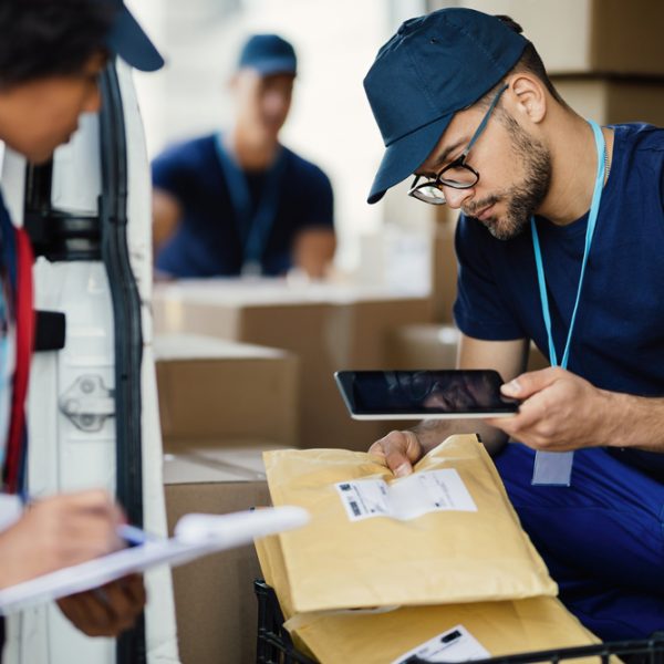 Two workers preparing packages for delivery and scanning bar cod Young delivery man using digital tablet for scanning bar code on package label while preparing for shipment with his coworker.